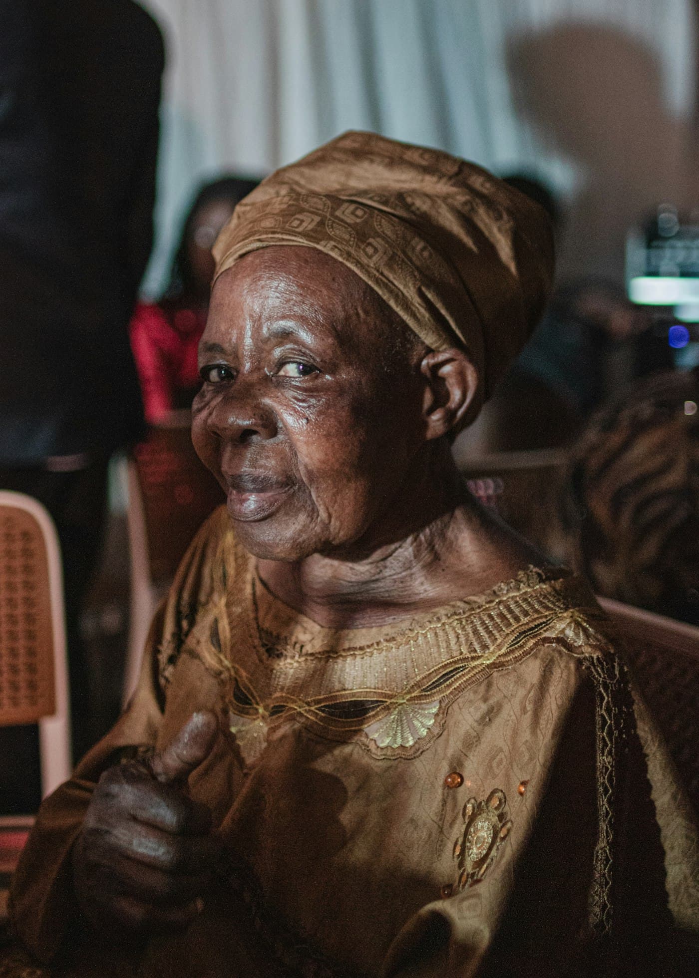 A smiling grandmother in a headwrap giving a thumbs up
