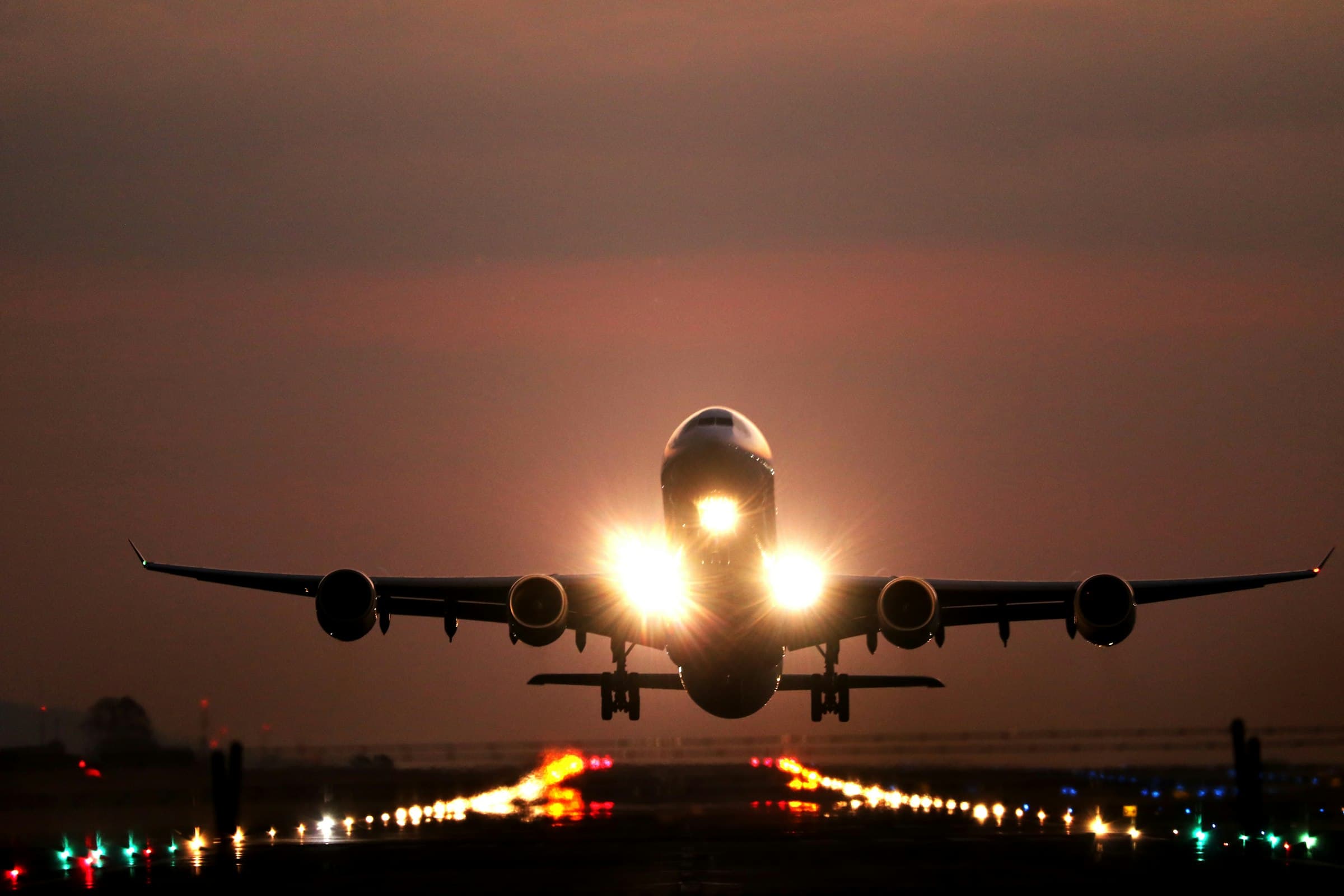 A passenger jet lifting off a runway at night with its landing lights on