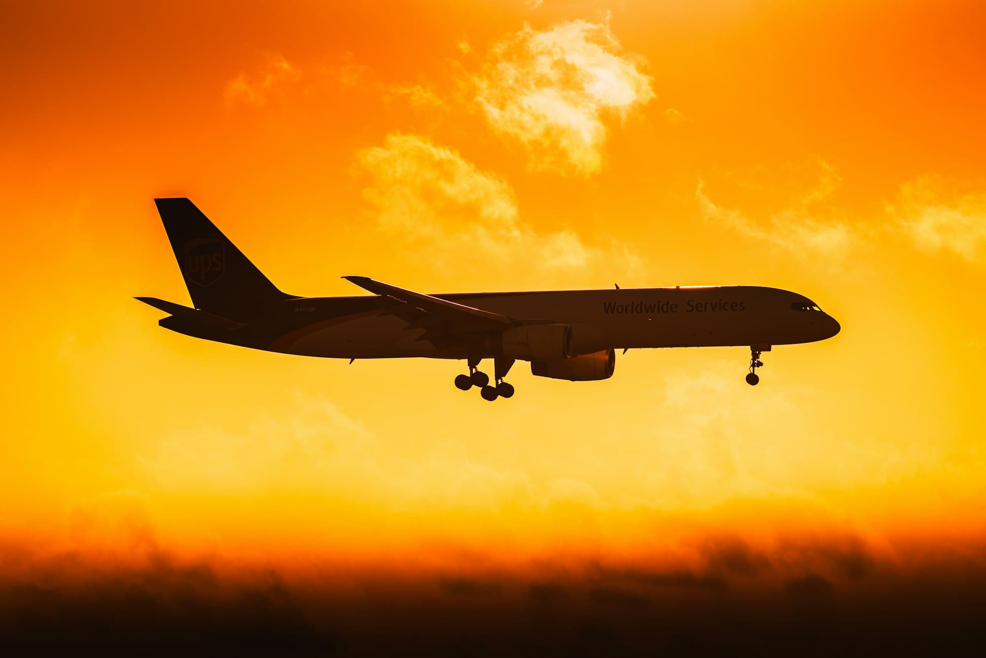 A cargo aircraft silhouetted against an orange sunset sky